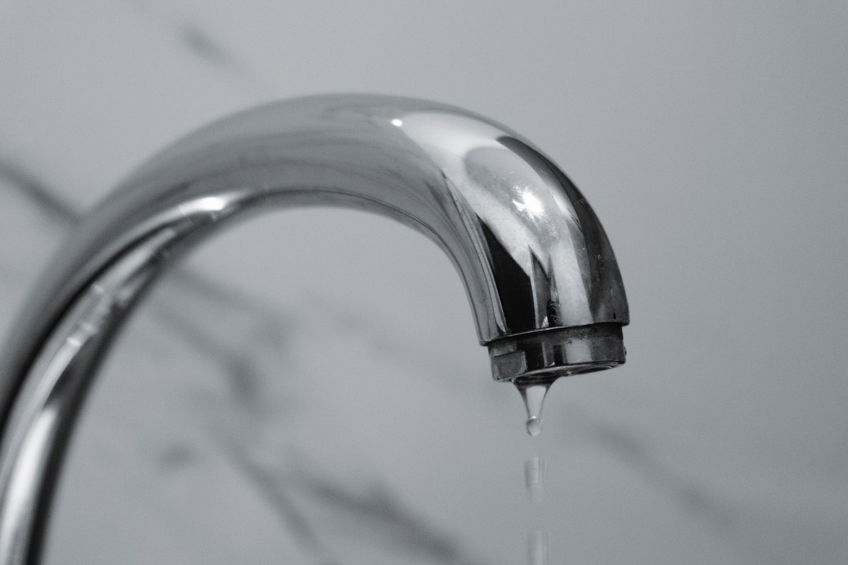 Licensed stock photograph: a drop of water hanging from the spout of a chrome faucet.