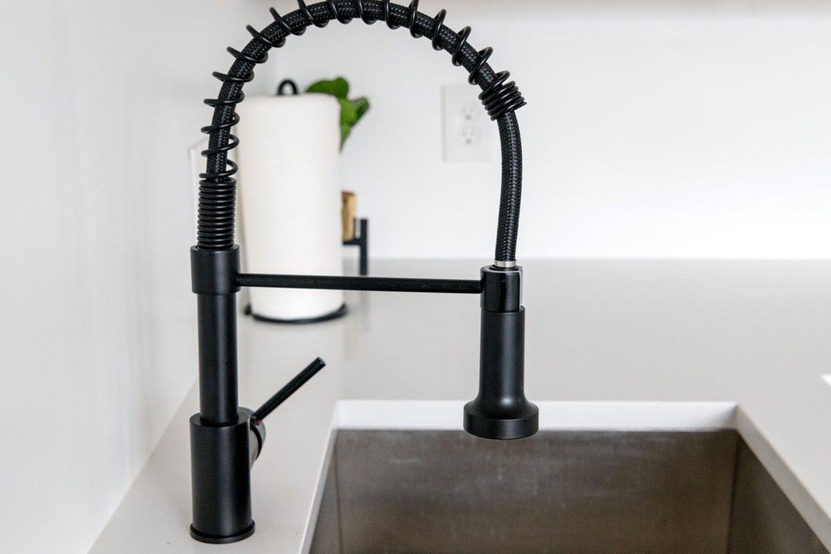 Licensed stock photograph: a black pull down faucet at a stainless steel kitchen sink.
